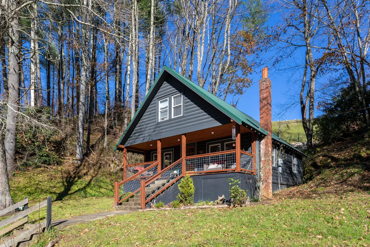 The hero image showcases a charming single-family cabin nestled among tall trees, with a welcoming front porch that invites guests to relax and enjoy the peaceful natural surroundings. The scene exudes tranquility, with the house set back from the road and enveloped in greenery, highlighting the cabin's secluded and inviting atmosphere.
