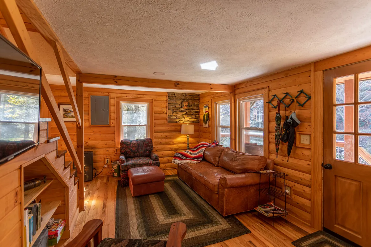 A living room scene with a plush leather sofa, a cozy armchair, and a rustic stone wall. Large windows bathe the space in natural light, creating an atmosphere ripe for relaxation, laughter, or enjoying board games with loved ones.