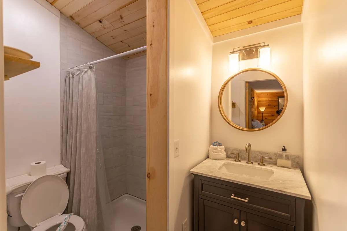 The bathroom features a modern walk-in shower, a sleek vanity with a round mirror, and calming, neutral tones. The space feels fresh, clean, and designed for personal rejuvenation, perfectly matching the description of the attached full bathroom.