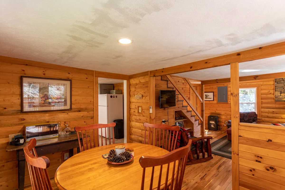 A warm interior space with a wooden dining table and chairs, visible staircase, television, and a fireplace in the background. The scene exudes a sense of togetherness and comfort, ideal for social gatherings, game nights, or family meals.